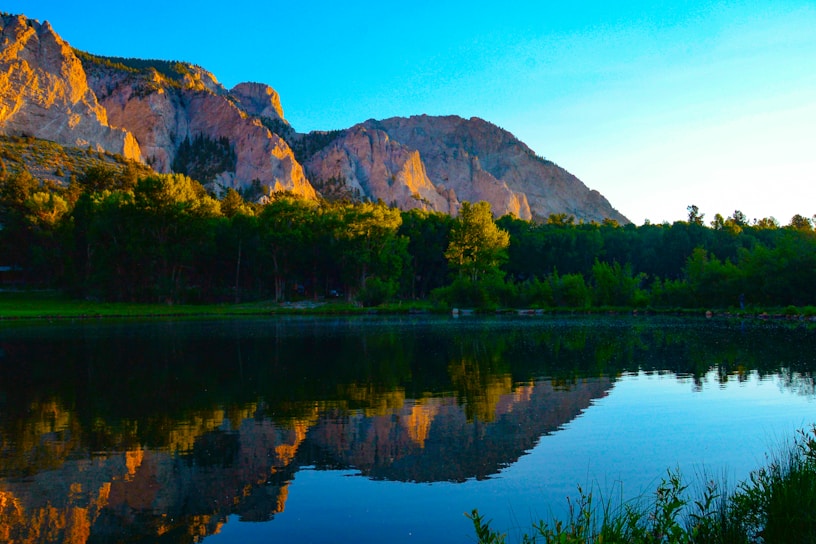 Golden hour sunlight bathes a serene mountain lake surrounded by lush pine trees.
