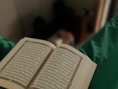 Close-up of hands holding a Quran with a delicate love symbol in the background.