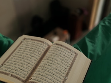 Close-up of hands holding an open Quran with soft natural light.