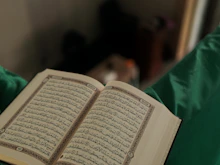 Close-up of hands holding the Quran with gold-accented decor softly blurred in the background.