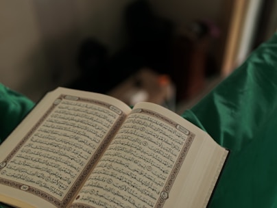 Close-up of hands holding an open Quran with soft natural light.