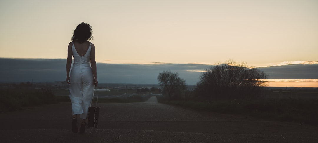 woman in white shirt standing on gray asphalt road during sunset