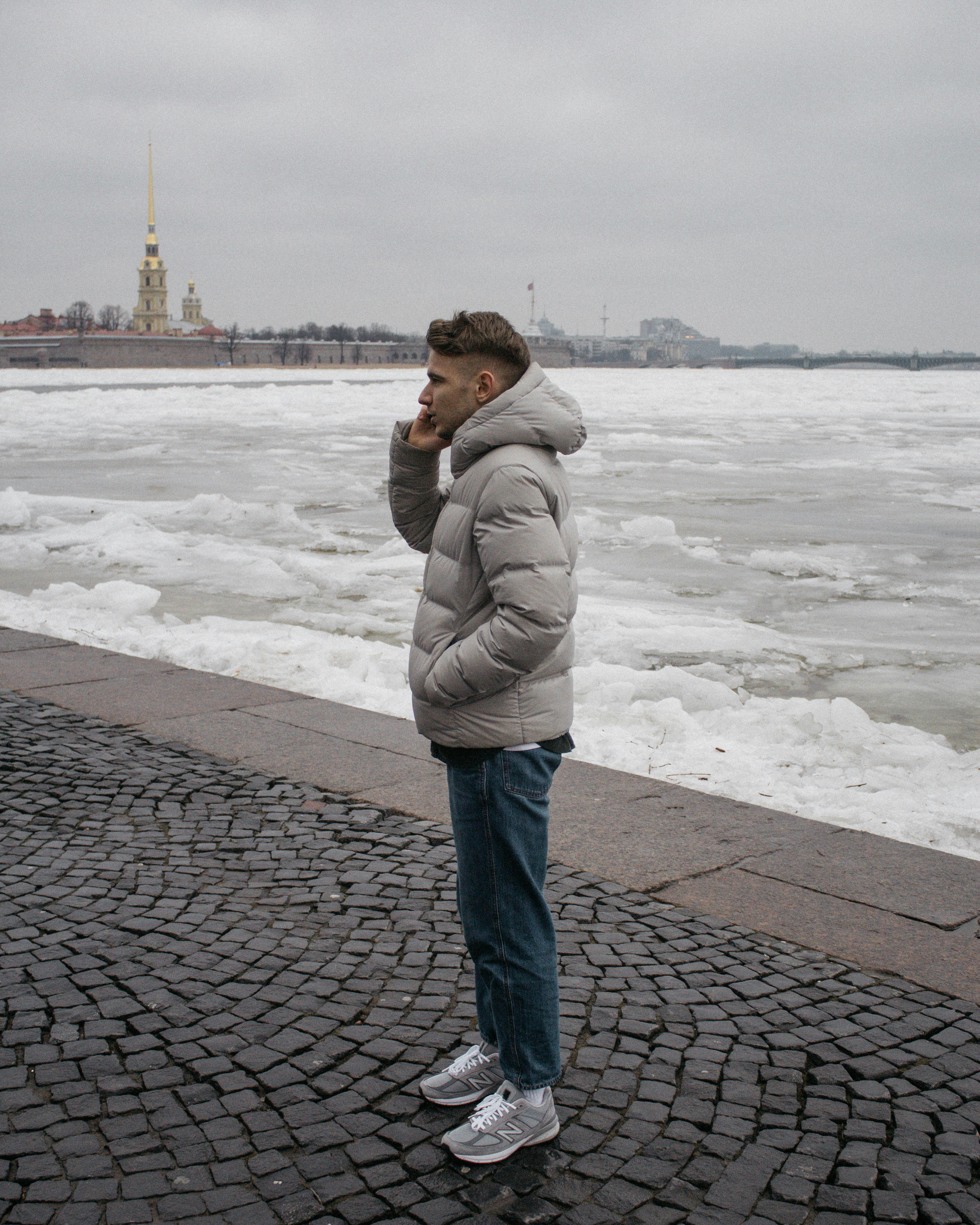 Femme en sweat à capuche gris debout sur un sol en briques grises près d’un plan d’eau pendant la journée