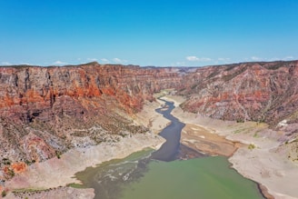 brown rocky mountain beside river under blue sky during daytime