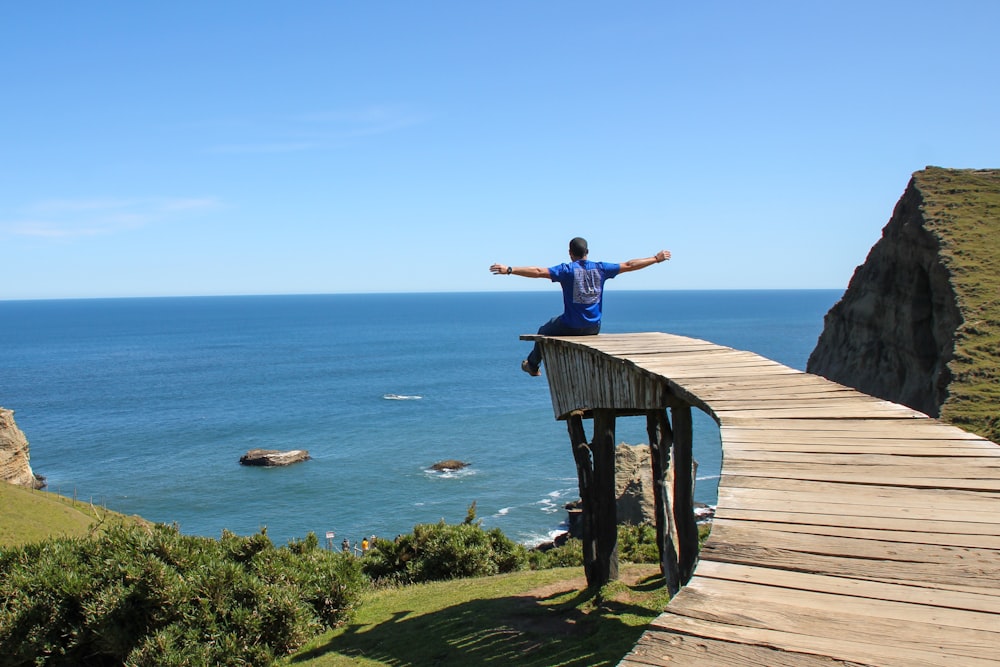 man in blue t-shirt and black pants standing on brown wooden dock during daytime