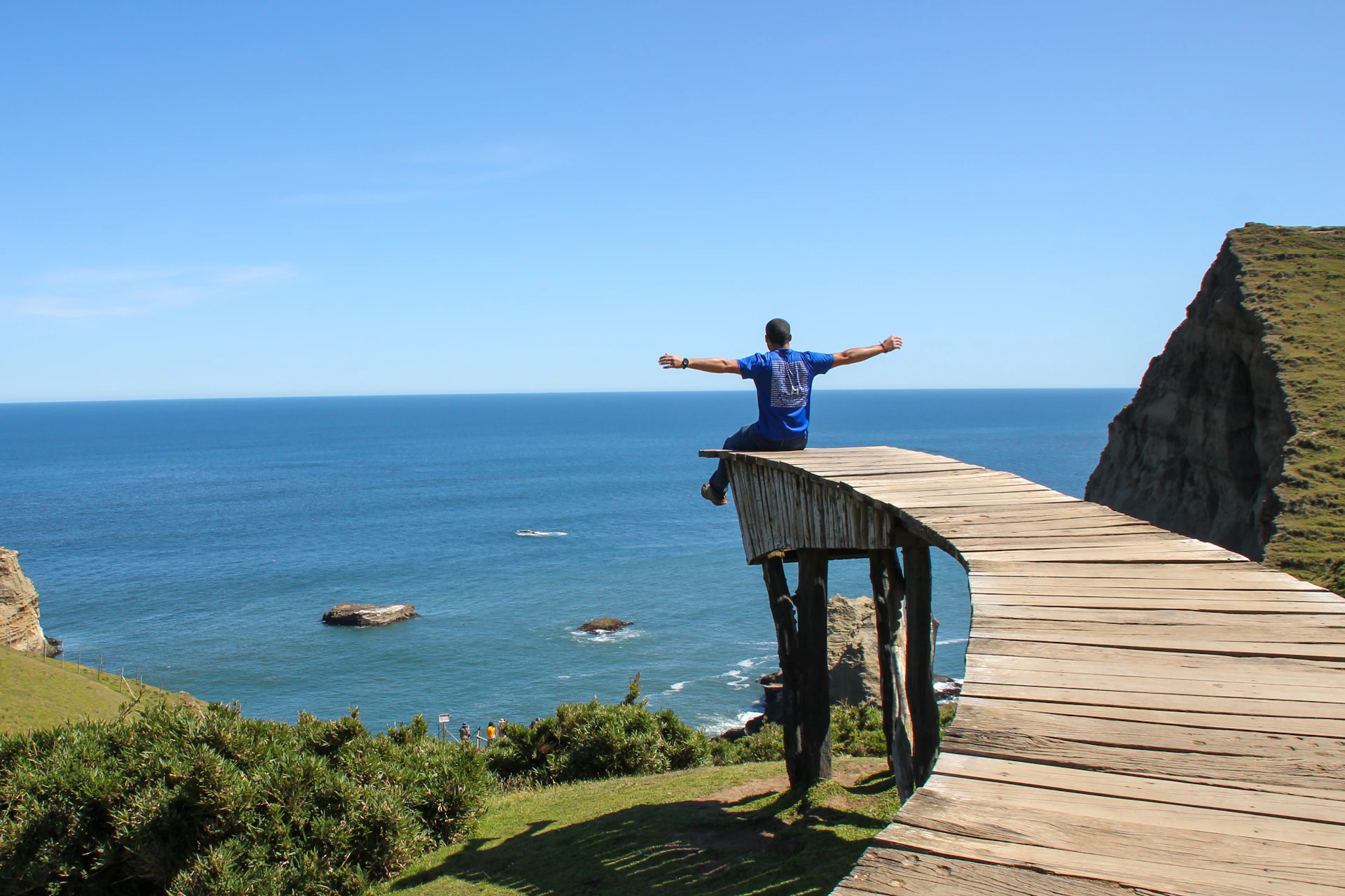 man in blue t-shirt and black pants standing on brown wooden dock during daytime