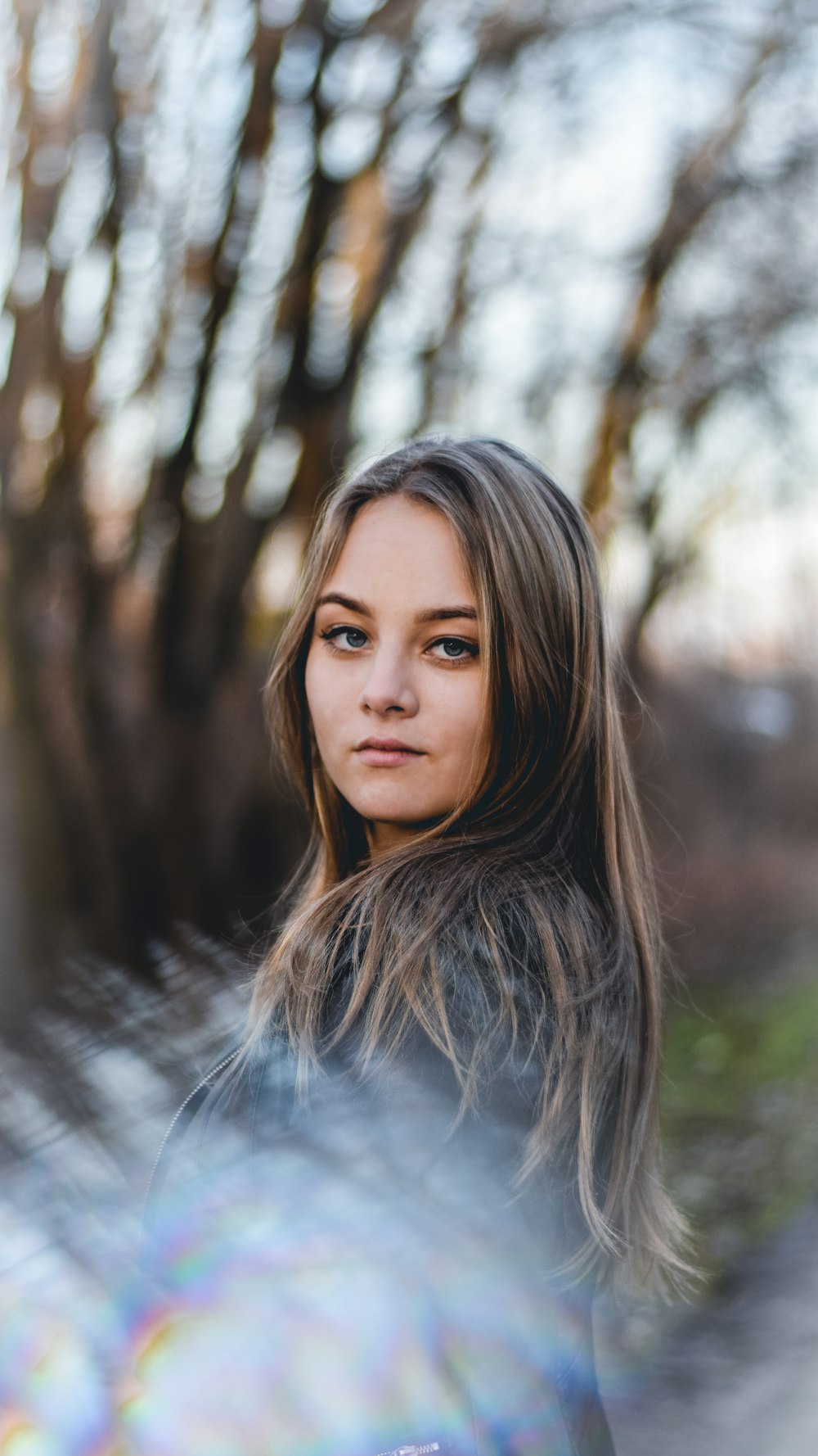 woman in grey shirt standing near brown trees during daytime