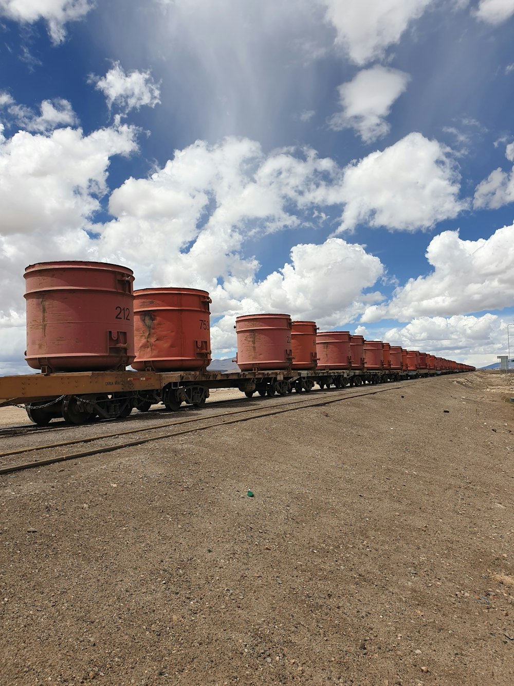 red steel barrels on gray asphalt road under blue and white sunny cloudy sky