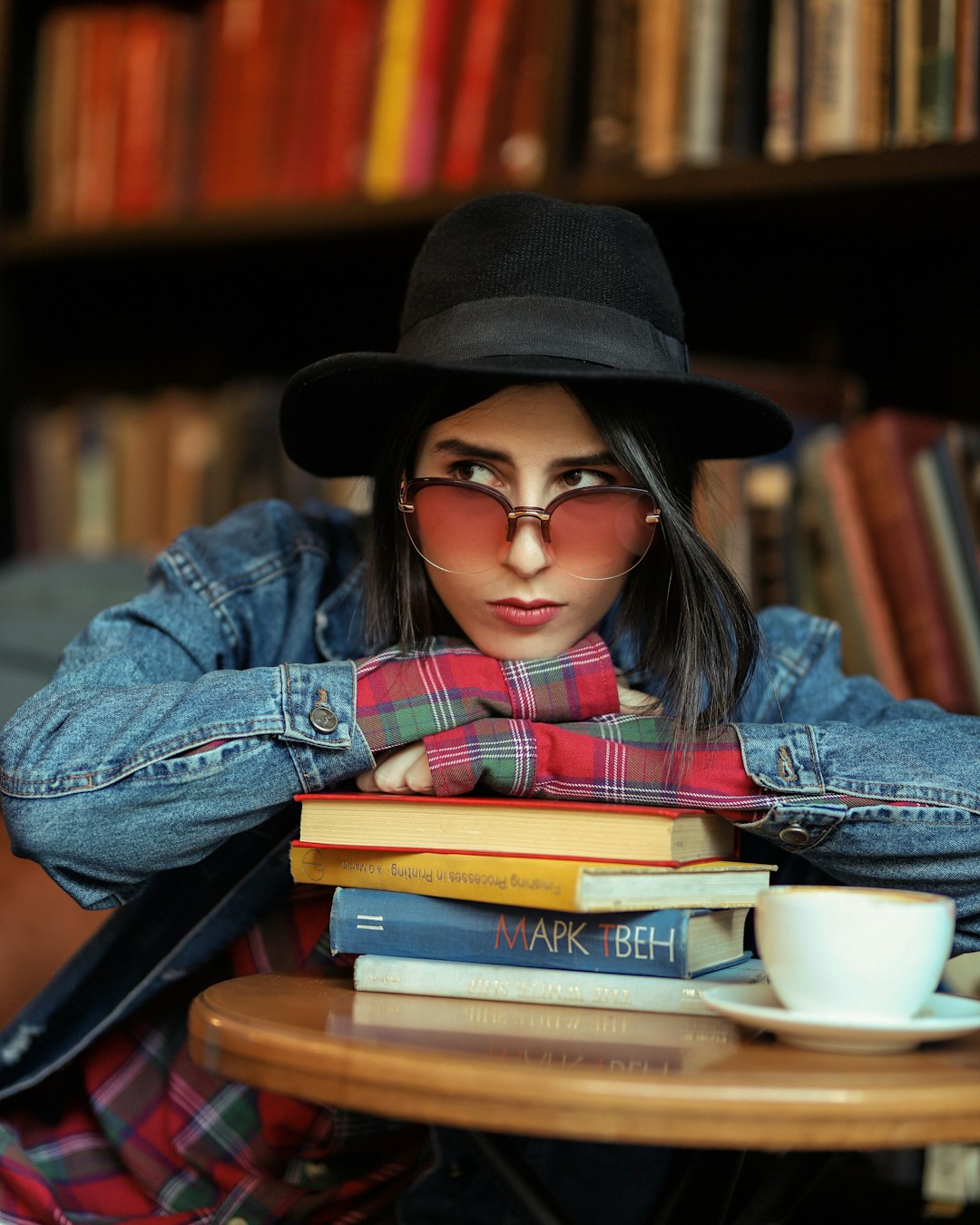 woman in blue denim jacket and brown fedora hat sitting on books