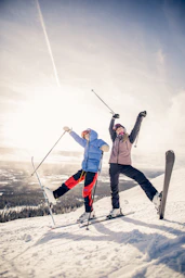 2 person in white pants and black snow ski blades standing on snow covered ground during