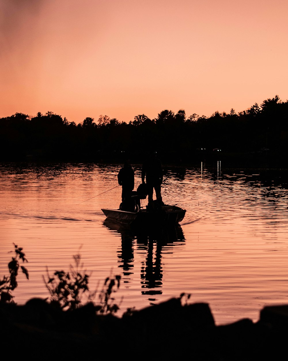 silhouette of 2 person riding on boat on body of water during sunset