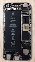 An open view of a smartphone revealing its internal components, including a prominent Li-ion battery and various microchips and circuits. The intricate hardware layout is visible with screws and connectors.