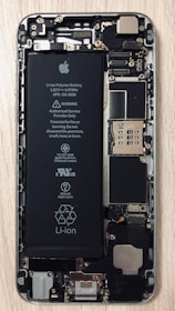 An open view of a smartphone revealing its internal components, including a prominent Li-ion battery and various microchips and circuits. The intricate hardware layout is visible with screws and connectors.