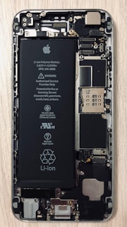 An open view of a smartphone revealing its internal components, including a prominent Li-ion battery and various microchips and circuits. The intricate hardware layout is visible with screws and connectors.