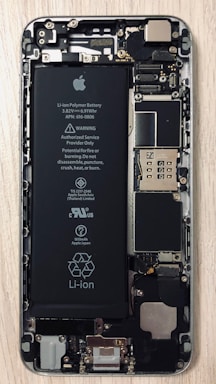 An open view of a smartphone revealing its internal components, including a prominent Li-ion battery and various microchips and circuits. The intricate hardware layout is visible with screws and connectors.