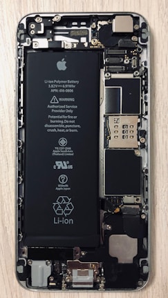 An open view of a smartphone revealing its internal components, including a prominent Li-ion battery and various microchips and circuits. The intricate hardware layout is visible with screws and connectors.