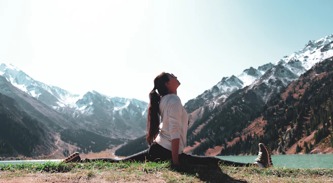 A serene morning scene with a person practicing yoga by a calm blue lake under a clear sky.