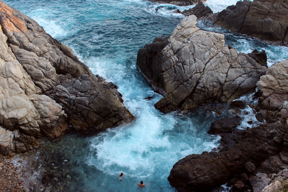 people surfing on sea waves crashing on rocky shore during daytime