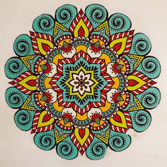 A vibrant, colorful mandala featuring intricate patterns and symmetrical designs. The mandala has a central flower-like motif surrounded by layers of geometric and floral shapes. The design is characterized by the use of bold lines and a variety of colors, creating a visually striking appearance.