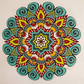 A vibrant, colorful mandala featuring intricate patterns and symmetrical designs. The mandala has a central flower-like motif surrounded by layers of geometric and floral shapes. The design is characterized by the use of bold lines and a variety of colors, creating a visually striking appearance.