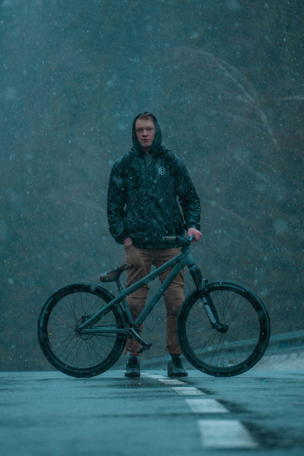 man in black jacket standing beside blue mountain bike