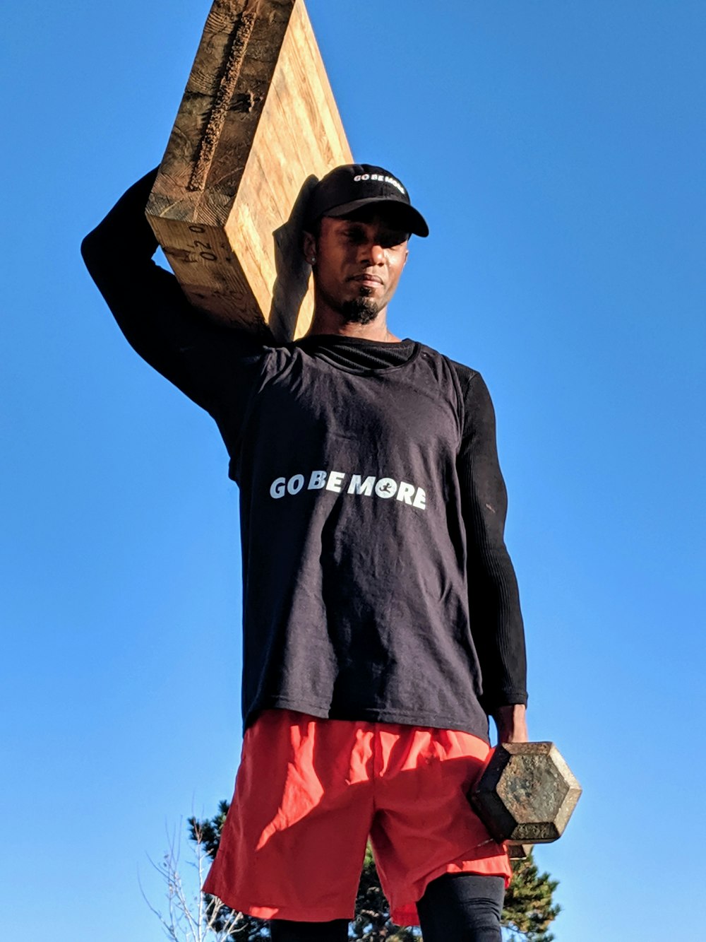 man in black long sleeve shirt and red shorts standing on brown wooden post