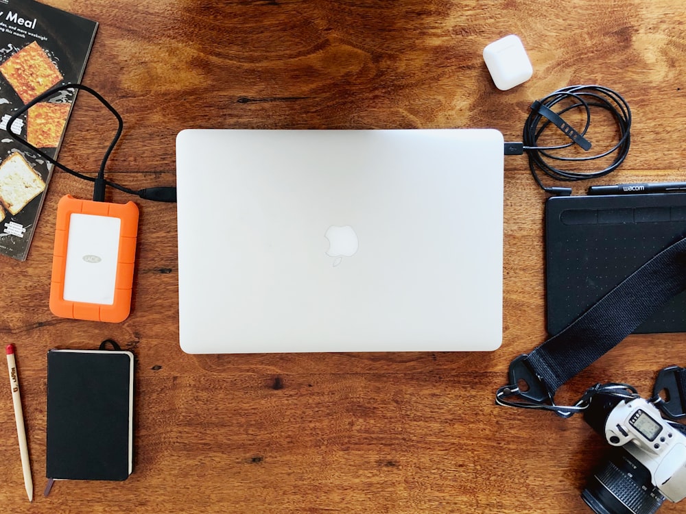 silver macbook beside black smartphone on brown wooden table