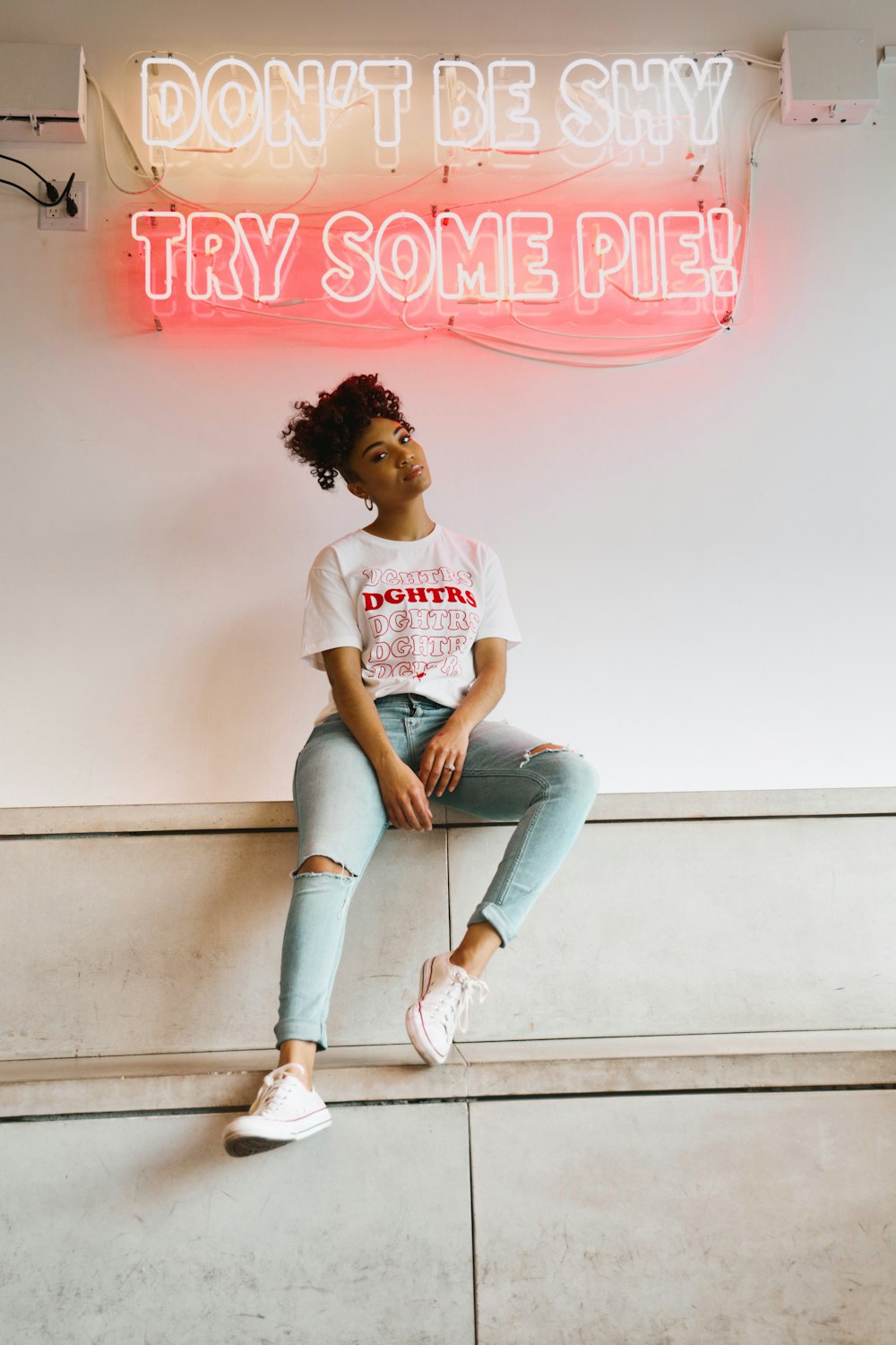 woman in white crew neck t-shirt and blue denim jeans sitting on white concrete wall