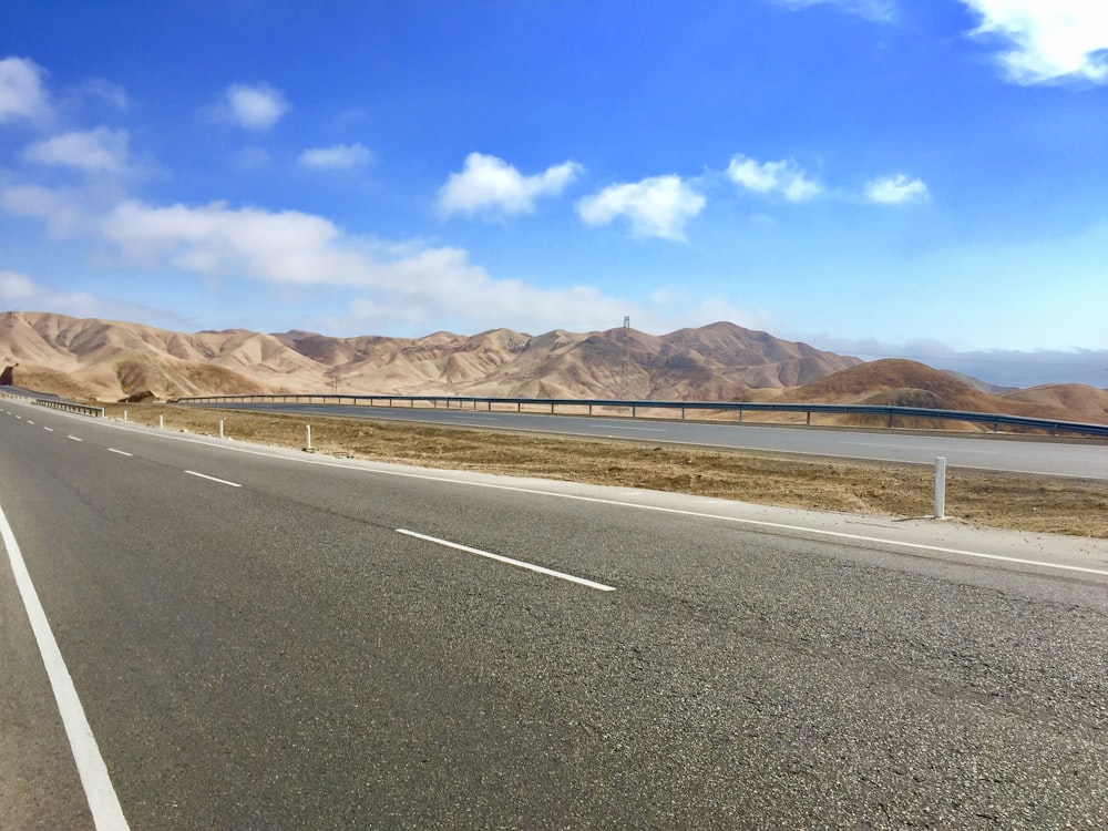 gray concrete road near brown mountain under blue sky during daytime