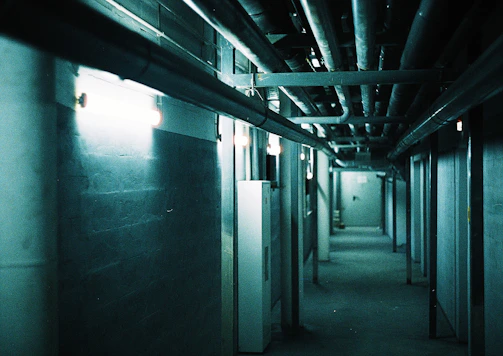 A dimly lit industrial corridor slick with rain and flickering fluorescent lights.