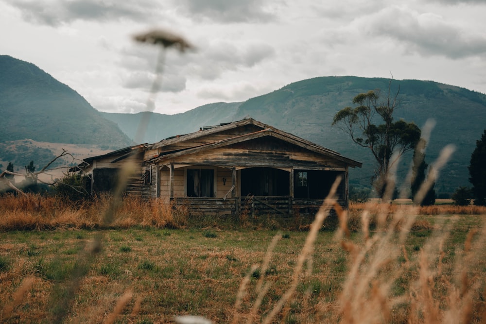 brown wooden house on brown grass field near mountain under white clouds during daytime