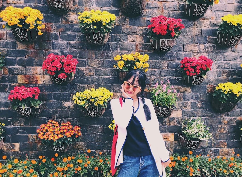 woman in white jacket and blue denim jeans standing beside red roses