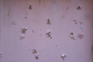 A textured wall with multiple areas of cracked and peeling paint, revealing darker surfaces underneath.