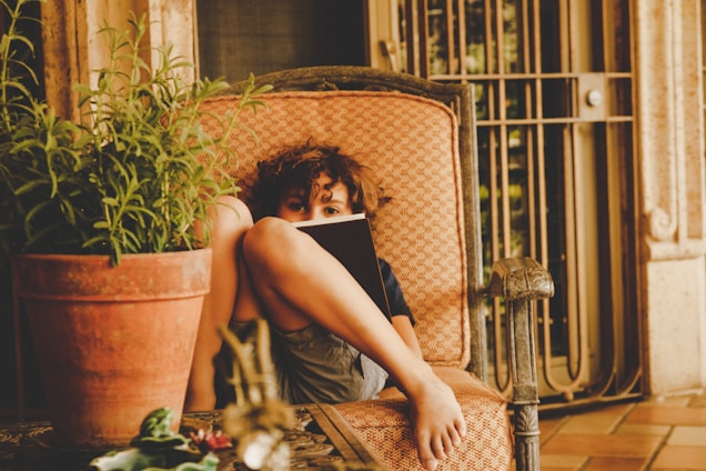 Kris C. Jefferson smiling warmly while holding a copy of Zoe’s Adventures with Elliot the Dragon in a cozy reading nook.