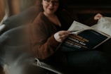 A person sits comfortably on a couch reading a newspaper. The newspaper features an advertisement for a career and graduate school fair. The lighting is soft and subdued, casting gentle shadows.