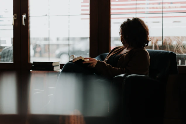Author sitting in a cozy, sunlit room surrounded by books and a laptop, writing with a calm expression.