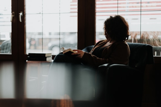 Amara Wisen sitting by a cozy window with a notebook, surrounded by books and soft light.