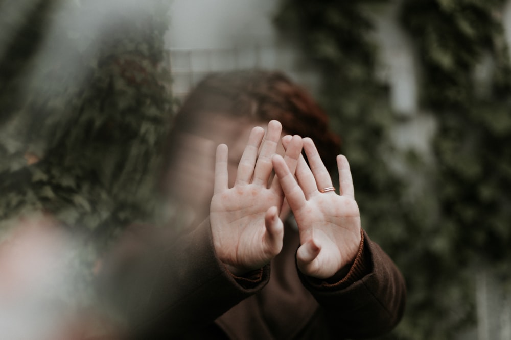 Person im braunen Langarmshirt, das Gesicht mit der Hand bedeckt