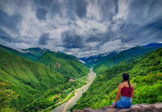 woman in blue tank top sitting on rock near green mountains under white clouds during daytime in Jujuy Argentina