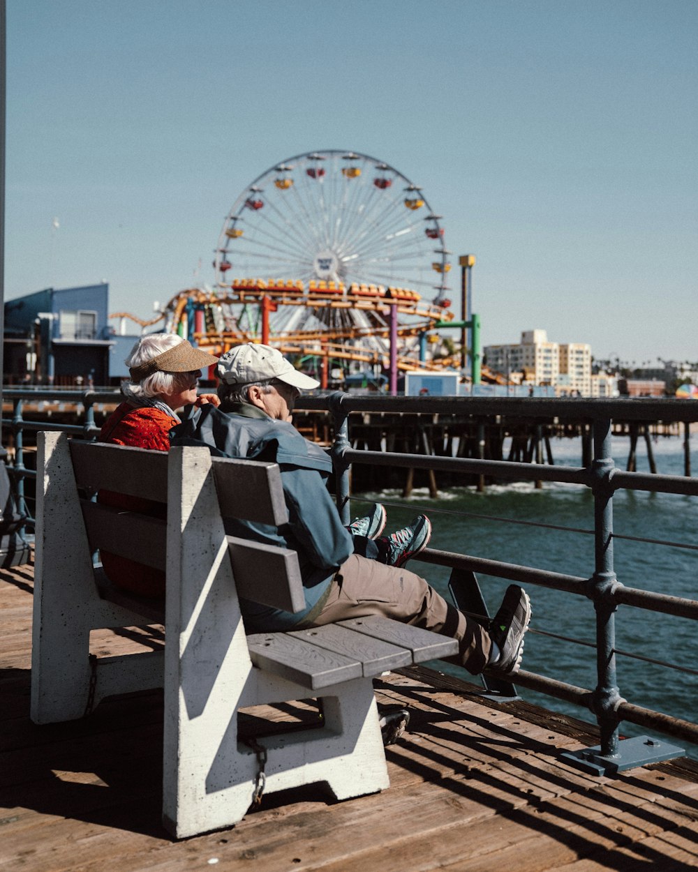 couple sitting on wooden bench near body of water during daytime