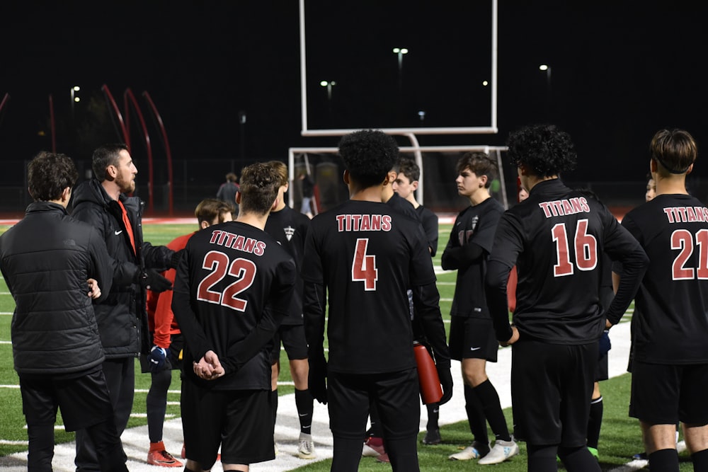 group of men in red and black jersey shirt standing on green grass field