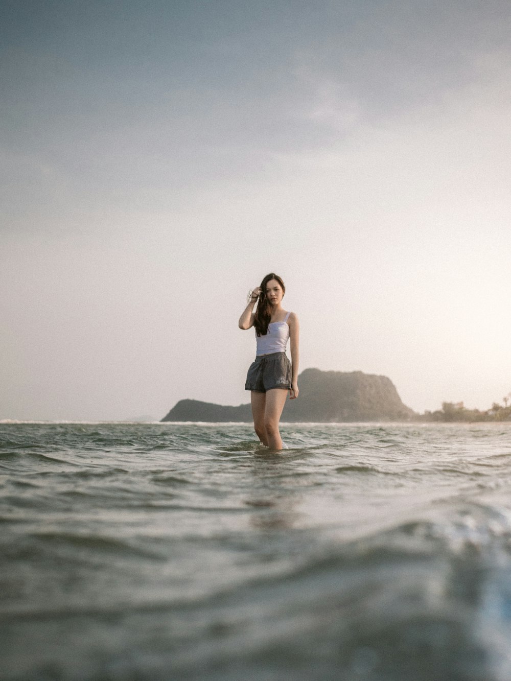 woman in black tank top and black shorts standing on rock formation on sea during daytime