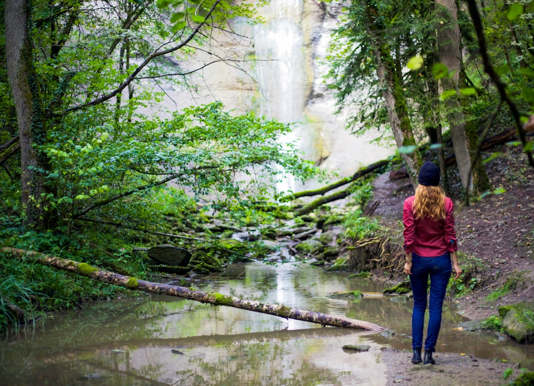 woman in red jacket standing near waterfalls during daytime