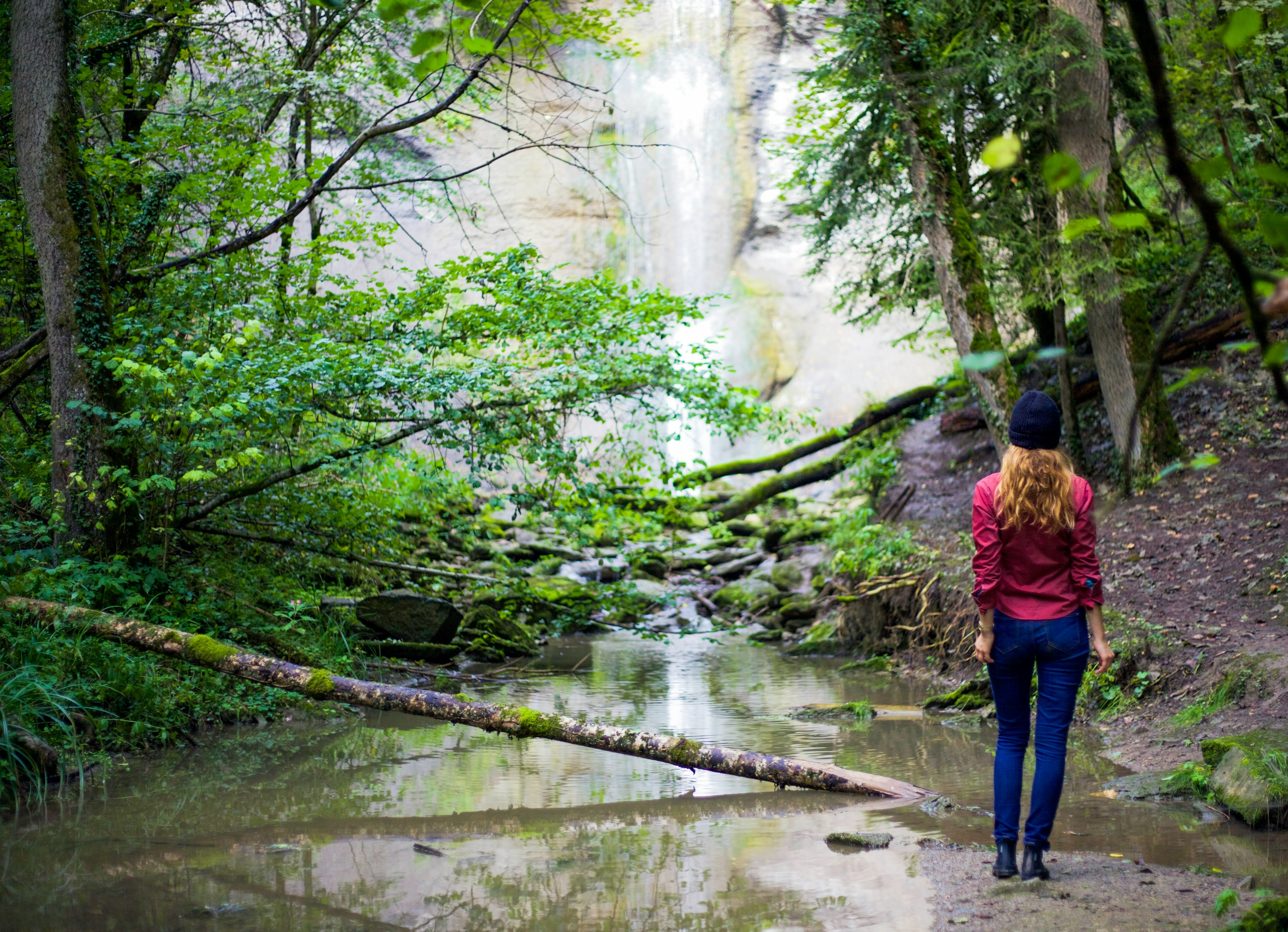 woman in red jacket standing near waterfalls during daytime