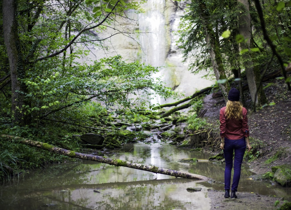 woman in red jacket standing near waterfalls during daytime