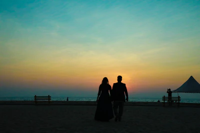 A sunset silhouette of a couple walking hand in hand along a quiet beach.