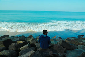 A person meditating on a rocky shore with waves gently crashing