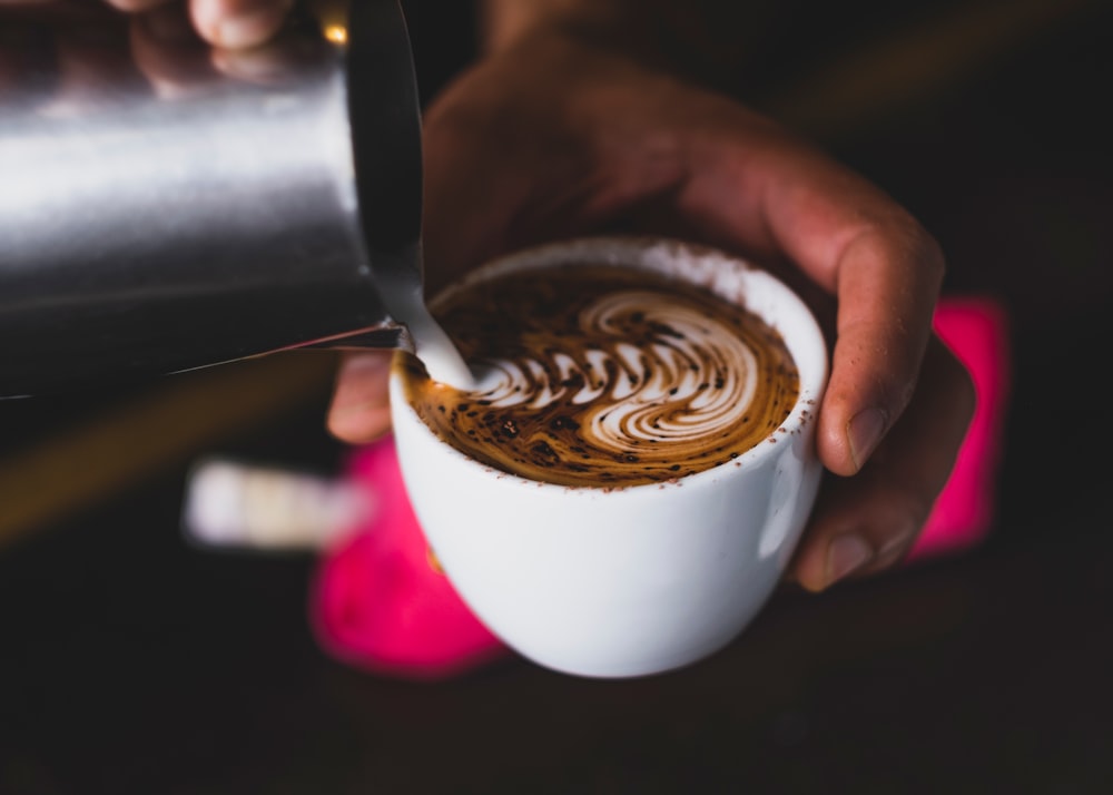 Person, die Kaffee auf weiße Keramiktasse gießt