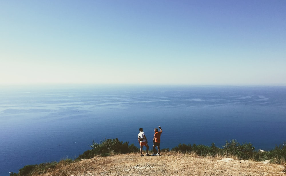 2 women and man standing on brown grass field near body of water during daytime