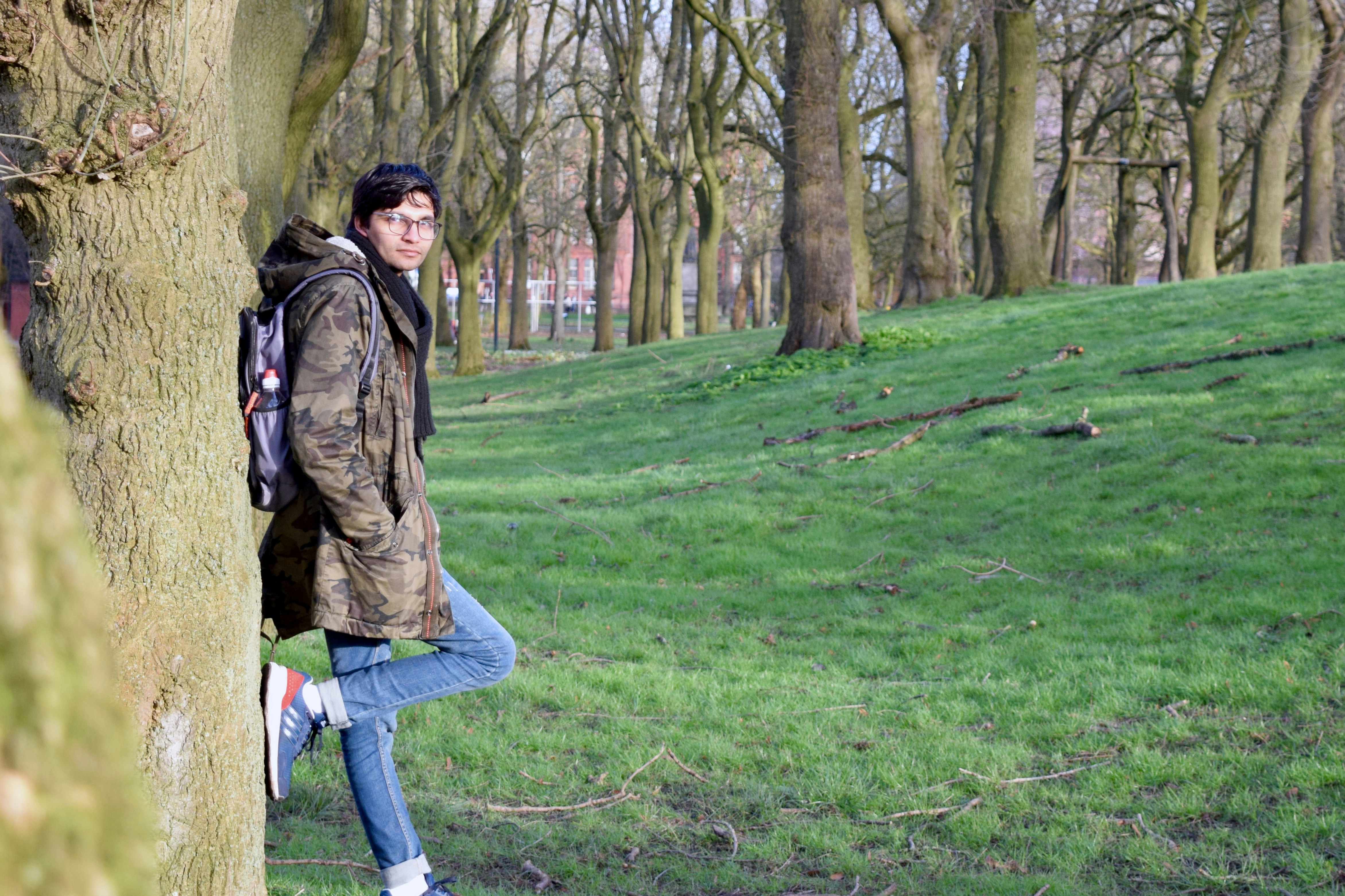 woman in brown jacket and blue denim jeans standing on green grass field during daytime